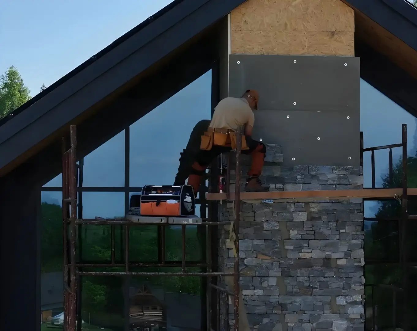Masonry expert, on the second story of a luxurious home, adds stone siding to the outside of a chimney.