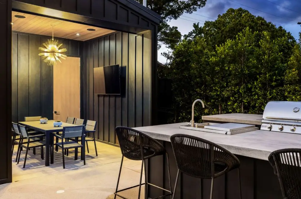 A modern outdoor kitchen with a grill, dining area, and stylish lighting in a sleek, contemporary design.