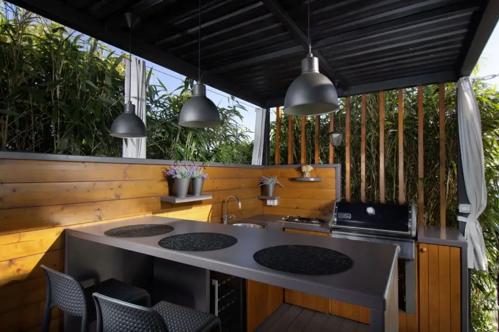 An open-air backyard mini kitchen featuring hardwood backsplashes, cabinets, stainless stoves, and countertops.