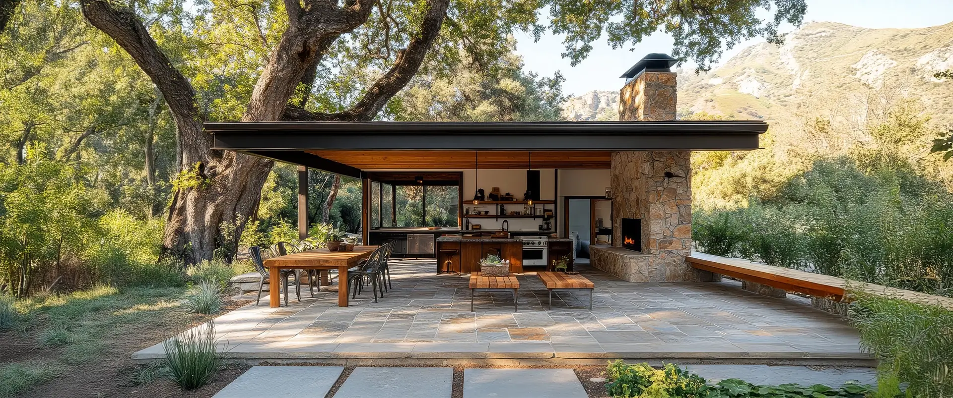 Traditional outdoor living space featuring an open-air kitchen, fireplace, and dining area with natural stone pavers.