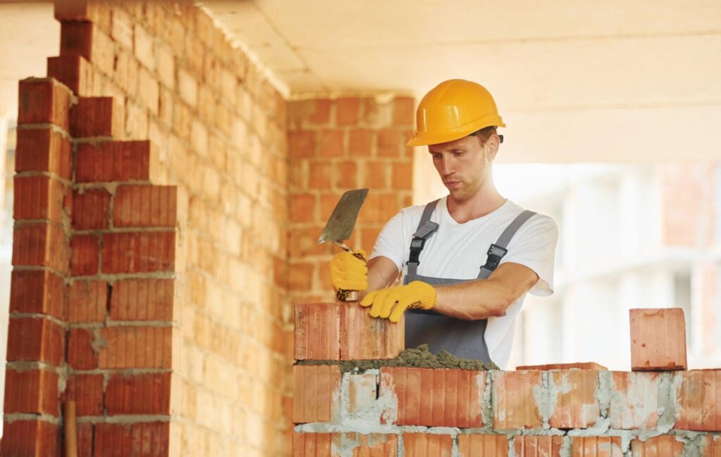 A young mason installs bricks at a construction site.