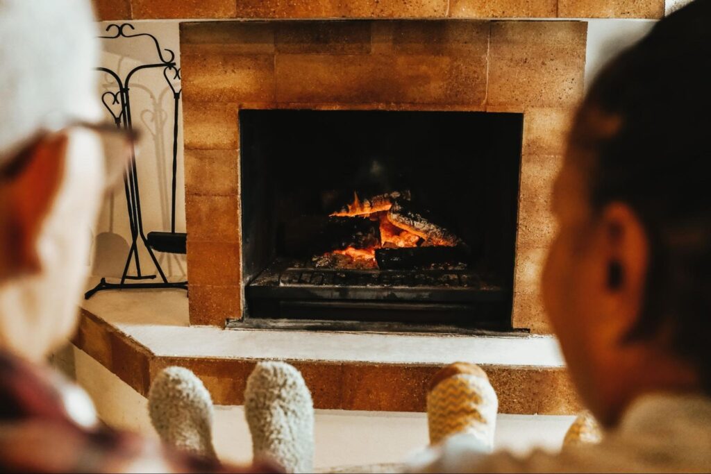 Rear view of two multiracial senior friends warming by the wood fireplace.