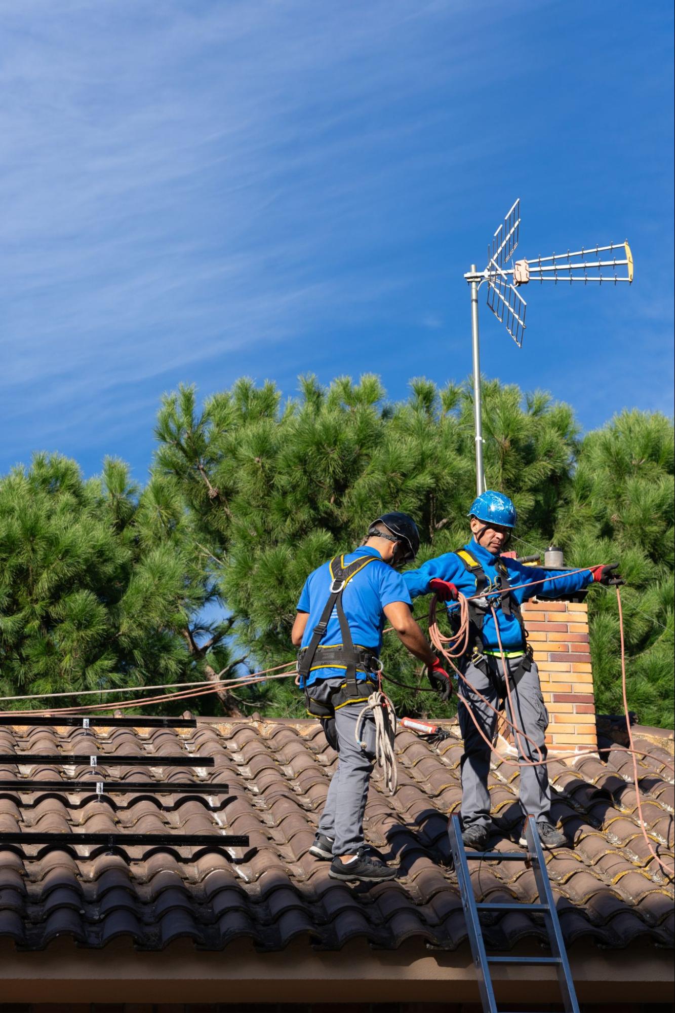 Two chimney technicians on a rooftop securing harness ropes before starting chimney repair work.