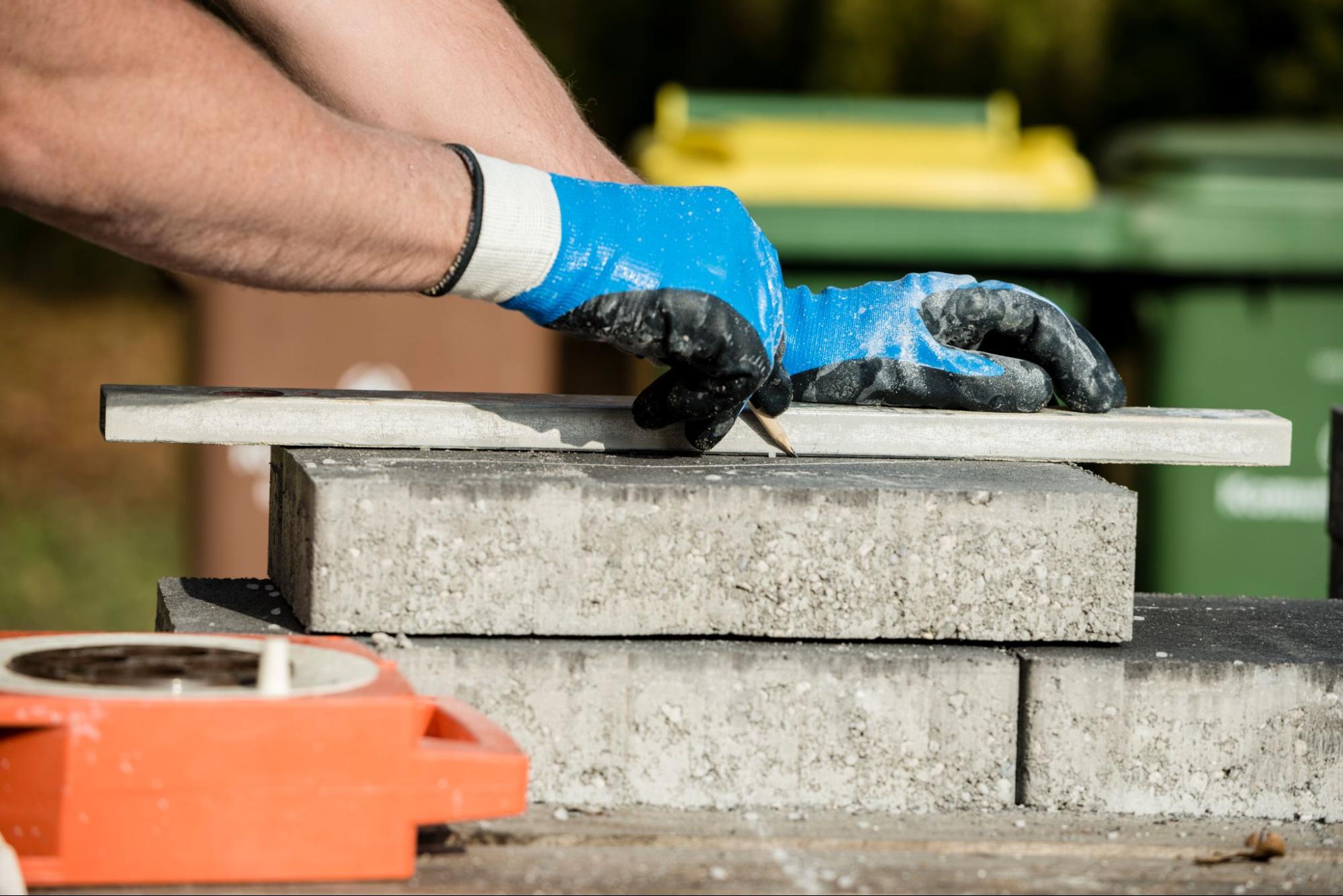 A builder marks a paving stone for precise cutting during masonry work.