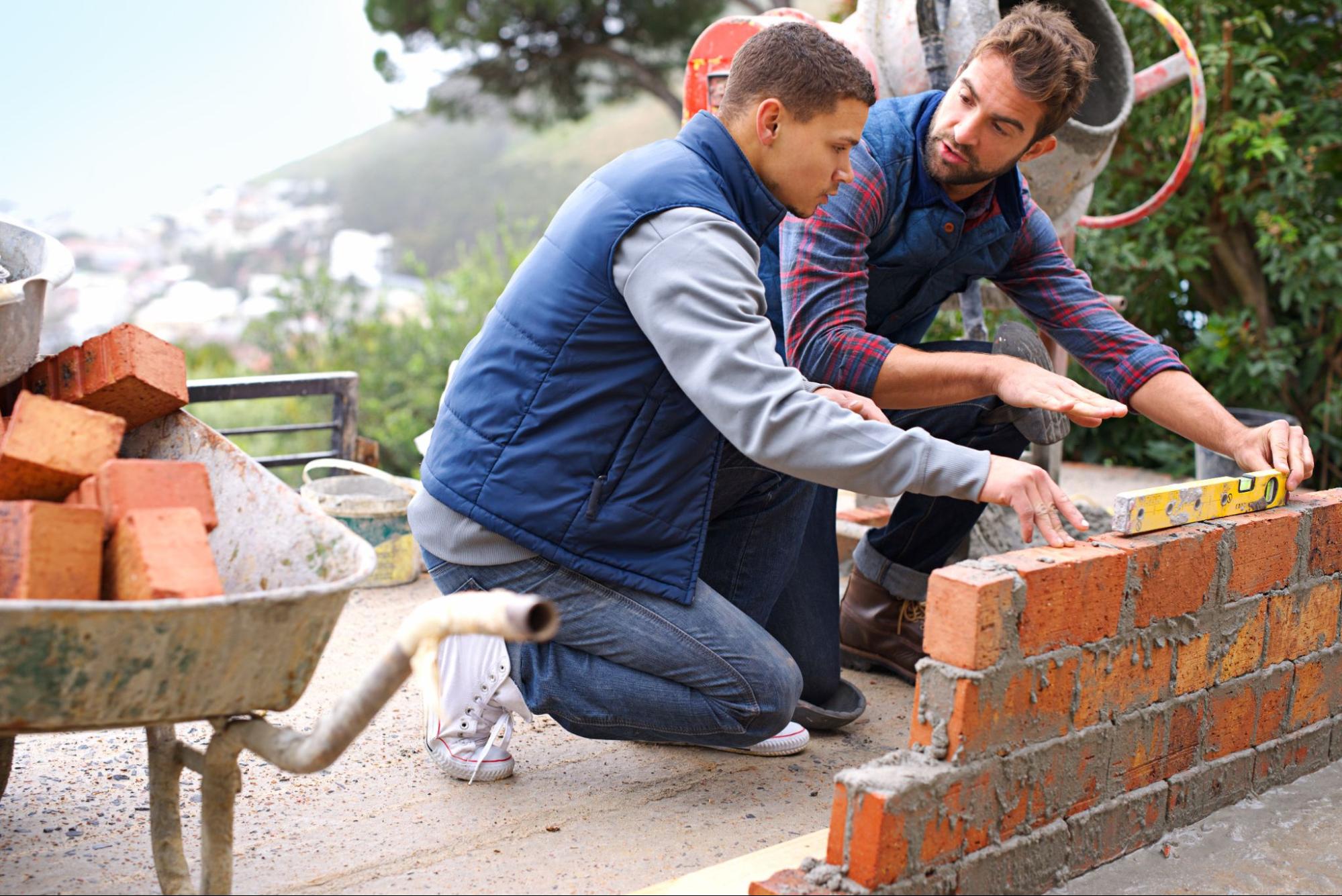 Skilled mason guiding a trainee through masonry work on-site.