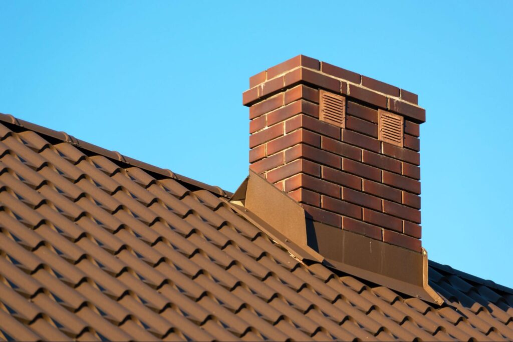 A brick chimney extending from a rooftop against a clear blue sky.