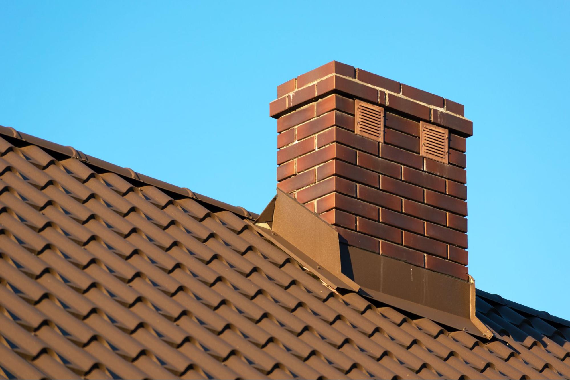 A brick chimney extending from a rooftop against a clear blue sky.