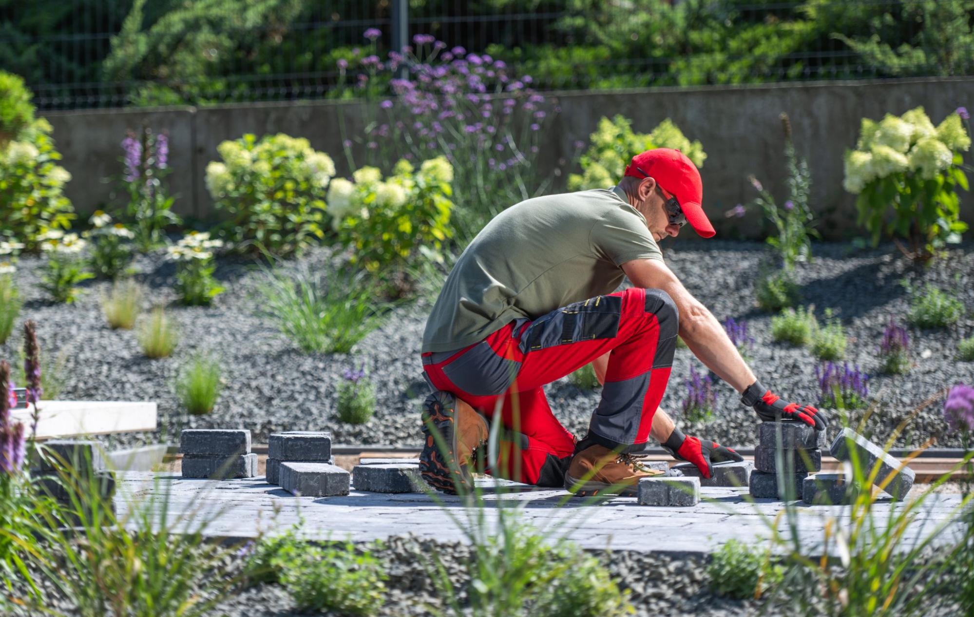 A masonry company specialist lays gray paving stones in a landscaped garden.