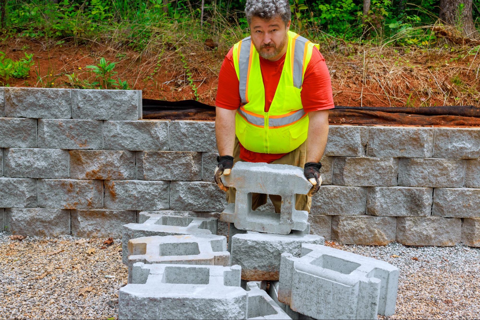 A masonry company worker lifts concrete blocks to build a retaining wall.