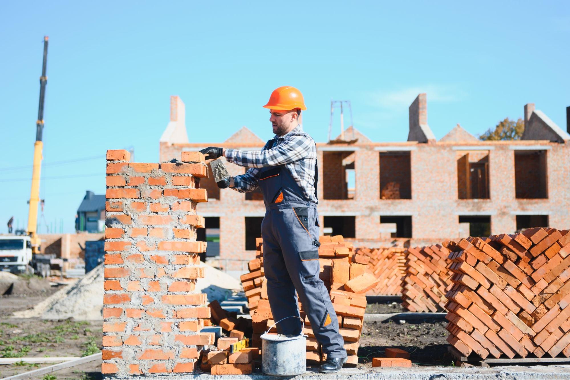 A masonry company worker in safety gear performs detailed brickwork.