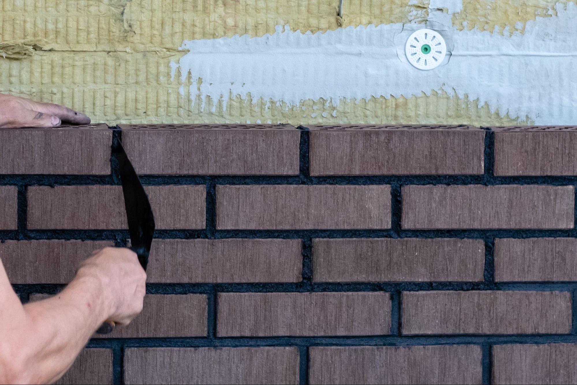 Closeup on a pair of hands installing brick veneer on a wall.