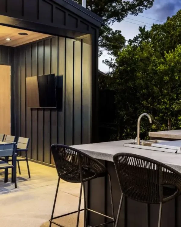 A modern outdoor kitchen with a grill, dining area, and stylish lighting in a sleek, contemporary design.