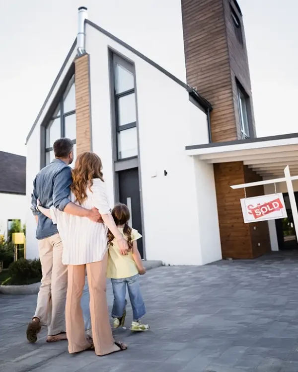 Back view of family near sign with sold lettering and house.