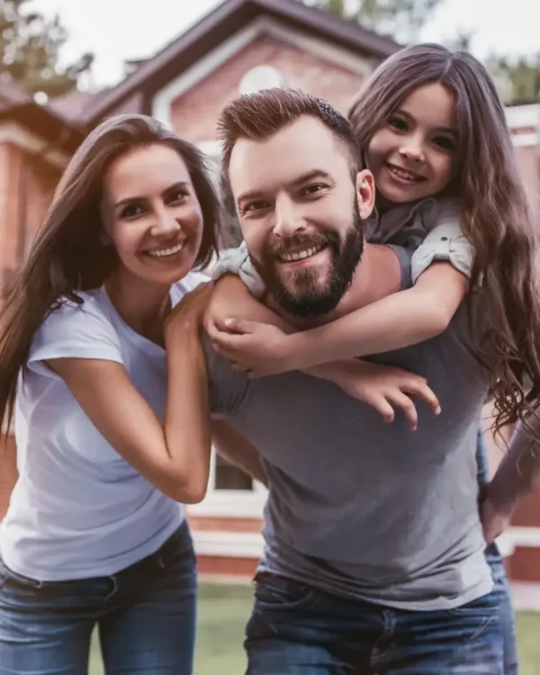 Happy family on their front yard smiling in front of their two story brick home.