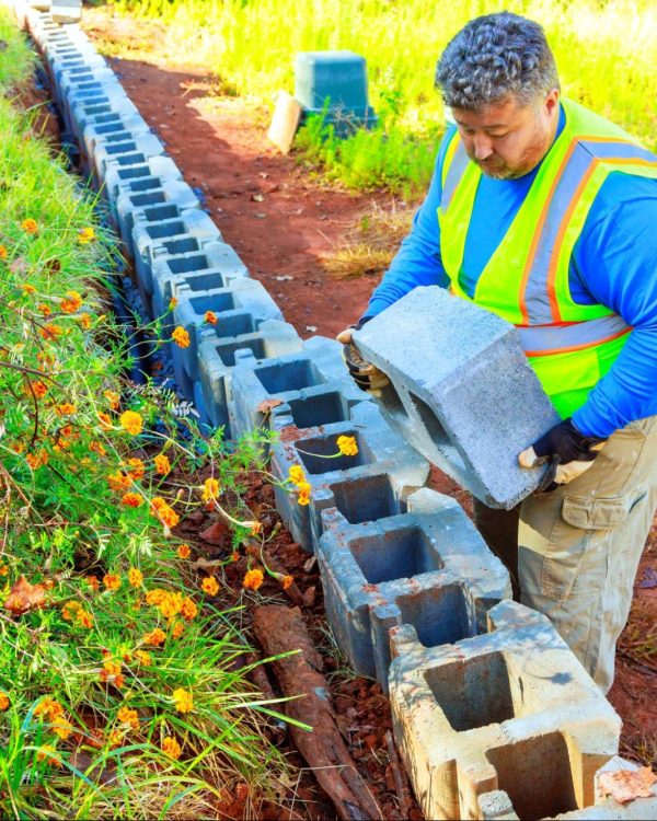 A construction worker stacks concrete blocks to build a retaining wall.